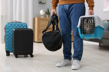 Travel with pet. Man holding carrier with cute cat and bag at home, closeup