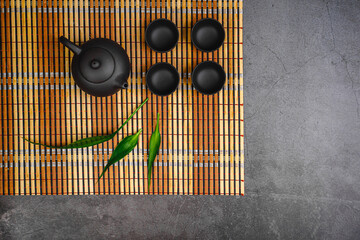Black teapot and cups with bamboo leaves on a tray. Traditional tea ceremony. 
Tea on a blue...