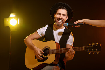 Naklejka premium Handsome man with acoustic guitar singing while woman holding microphone on dark background, closeup