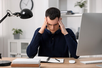 Young man suffering from headache at workplace in office