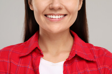 Young woman with clean teeth smiling on light grey background, closeup