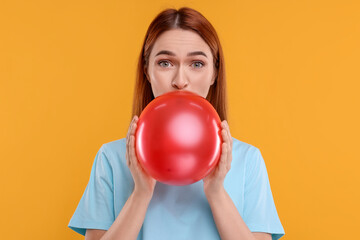 Woman inflating red balloon on orange background