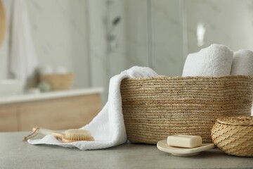 Wicker basket with clean towels and massage brush on table in bathroom