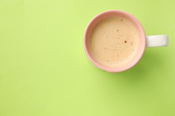 Aromatic coffee in cup on light green background, top view. Space for text