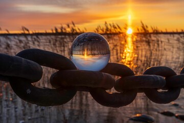 Glass lens on an old chain overlooking the tranquil ocean waters at sunset.