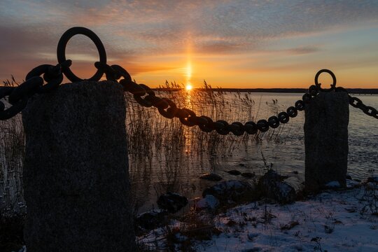 Old, rusted chain stretched across a tranquil body of water at sunset.