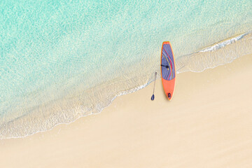 Top view of SUP board for surfing on the shore on tropical Seychelles sand beach. Blue, turquoise transparent water surface of ocean, sea, lagoon. Aerial, drone view