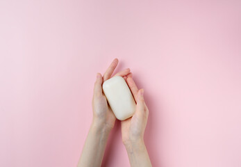 Woman's hands holding a soap on pastel pink background. Top view, flat lay.