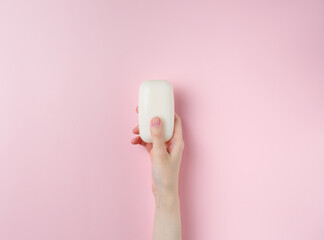 Woman's hands holding a soap on pastel pink background. Top view, flat lay.