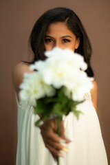 Young woman in a white dress, holding a bouquet of white flowers up to her face with a smile