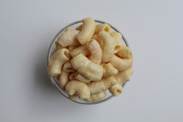 Fried macaroni crackers, on a transparent glass bowl, isolated on white background