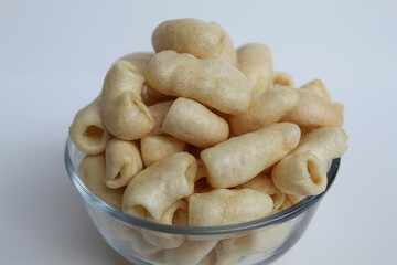 Fried macaroni crackers, on a transparent glass bowl, isolated on white background