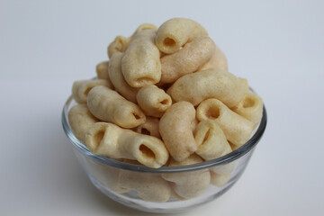 Fried macaroni crackers, on a transparent glass bowl, isolated on white background
