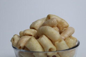 Fried macaroni crackers, on a transparent glass bowl, isolated on white background