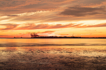 Beautiful sunset on the beach with container cranes visible
