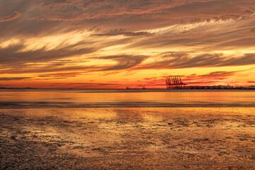 Fototapeta na wymiar Beautiful sunset on the beach with container cranes visible 