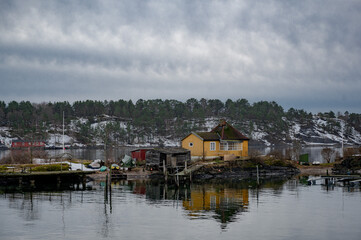 Fototapeta na wymiar A wooden Norwegian cottage on the shore of the Oslo fjord on a winter day. Yellow house on the shore
