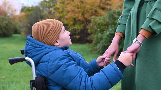 a 10-year-old disabled child in a wheelchair on the street with his mother for a walk. in autumn. High quality FullHD footage