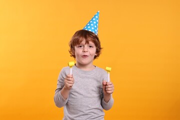 Birthday celebration. Cute little boy in party hat with blowers on orange background
