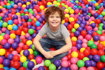 Fototapeta na wymiar Happy little boy sitting on colorful balls in ball pit