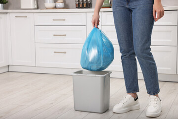 Woman taking garbage bag out of trash bin in kitchen, closeup. Space for text