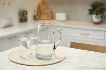 Fototapeta na wymiar Jug and glasses with clear water on white table in kitchen, space for text