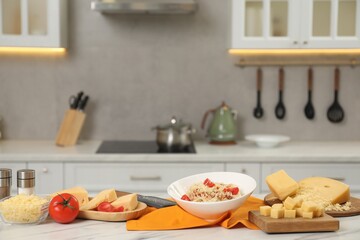 Delicious pasta with grated cheese and tomatoes on white marble table in kitchen