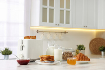 Making toasts for breakfast. Appliance, crunchy bread, honey, jam, milk and croissant on white marble table in kitchen - obrazy, fototapety, plakaty