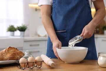 Making bread. Man putting flour into bowl at wooden table in kitchen, closeup
