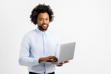 Smiling african businessman using laptop, standing at white backdrop, checking home finance, happy man looking at invoice, looking at camera, connection with bank, checking bill using online app