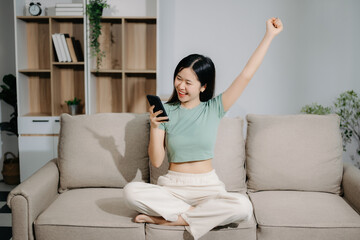Obraz premium Young asian woman using smartphone and tablet while seated on couch at home.