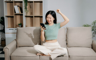 Obraz premium Young asian woman using smartphone and tablet while seated on couch at home.