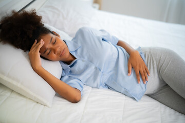 Top view of Young African American pregnant woman lay on bed, have an head ache with eye bow fold...