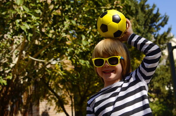 Cute little preschooler boy holding a yellow soccer ball. A child in sunglasses holds a ball, laughs