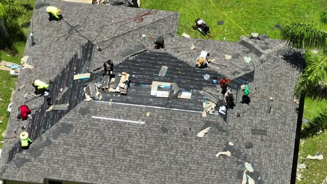 Construction workers installing asphalt shingles as house roof covering. Building of Florida home rooftop. Real estate development concept