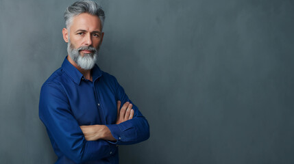 Homem mais velho de barba vestindo uma camisa azul de braços cruzados isolado no fundo cinza