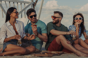 Group of happy young people enjoying pizza and beer while spending time on the beach together