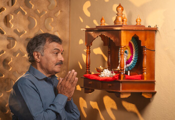 devotional indian senior man worshipping by praying in front of god at home during morning by...