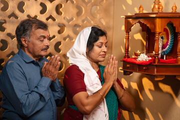 Devotional Indian elderly couple praying to god in front of mandapam during morning - concept of...