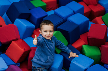Little boy, happy smiling child lying down playing with soft colored cubes in playroom, showing...