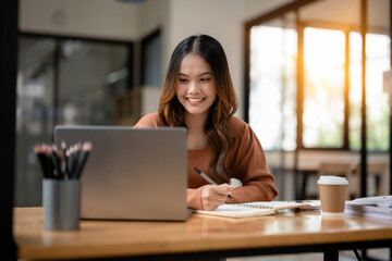 Cheerful young woman in casual attire focusing on a laptop screen, working from a modern office.