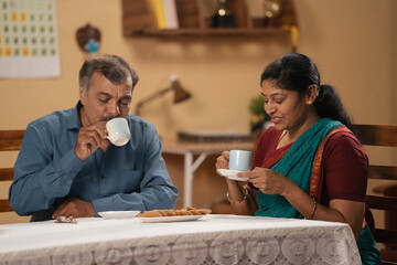 Happy senior couples enjoying morning tea with biscuits by talking each other at home - concept of retirement lifestyles, freedom and refreshment.