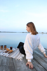 the girl sits on a wooden pier near the lake. aesthetic photo. picnic on a wooden pier with coffee and croissants