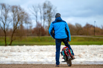 A man on an electric unicycle stands by the river and watches the ice break in the spring © ako-photography