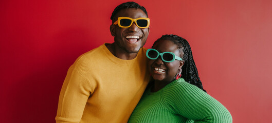 Fashionable young African couple in trendy glasses embracing and smiling on red background together - obrazy, fototapety, plakaty