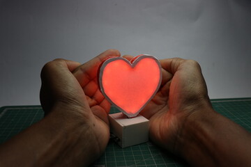 LED heart made using 3D print technology being covered with hands showing the concept of protected...
