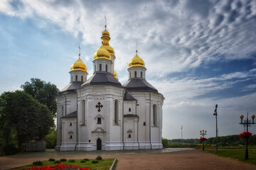 Fototapeta na wymiar The ancient Orthodox Church of St. Catherine, a resplendent white church with gilded domes and crosses, as it stands against the serene blue sky with soft, billowing clouds.