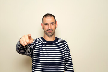 Portrait of handsome man in his 40s pointing index finger at you over isolated beige background, looking at camera. A friendly, smiling guy pointing his index finger at the camera choosing you