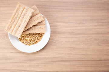 Buckwheat crisp bread and buckwheat on plate on wooden background, gluten free. Dietary cookies