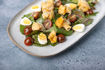 Warm salad with rapan (snails), tomatoes, cucumbers, leafy vegetables, quail eggs and olive oil. Traditional seafood salad. Close-up, selective focus.